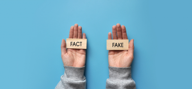 Zwei Hände halten die Wörter "Fake" und "Fakt" auf blauem Hintergrund